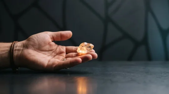 Une main tenant délicatement un fragment de verre lumineux en équilibre sur une surface sombre, symbolisant la tension entre viralité et cohérence de marque